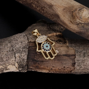 Detailed view of a golden Hamsa Hand pendant with zircon Evil Eye on a natural branch