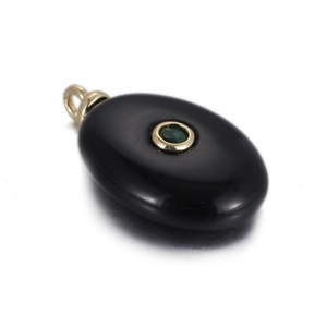 Macro shot of oval black stone pendant with green zircon inlay and gold plating