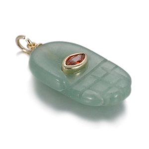 Macro detail of hand-shaped green jade pendant with inlaid garnet and gold metal ring