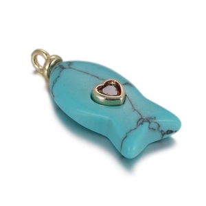 Macro view of turquoise fish pendant with red heart gemstone and gold hanging loop