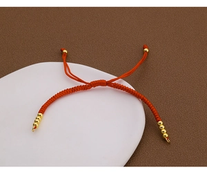 Detail eines roten handgeflochtenen Armbands mit Goldperlen auf weißem Display