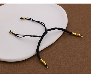 Detail eines handgewebten schwarzen Kordelarmbands mit Schiebeknoten und Goldperlen