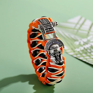 Detailopname van het oranje paracord-vlechtwerk en de zilveren Spartaanse helm-bedel