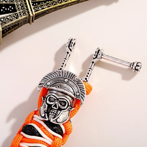 Detail van paracord armband met een schedelbedeltje en geweven oranje koord