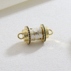 Macro detail of gold cylinder charm with white enamel, star patterns and colorful crystals