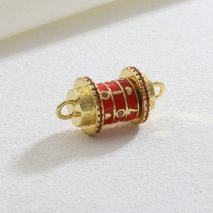 Detail of a luxury gold-plated cylinder charm with red enamel and small orange rhinestones