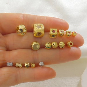Detalle de dijes de cobre chapados en oro de 18k con circonitas de colores en la mano