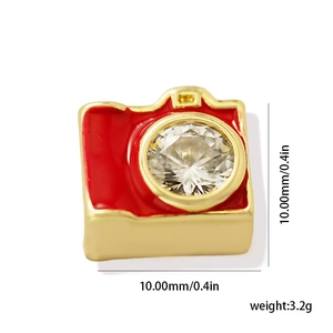 Detail view of a 10mm gold camera charm with red enamel and a clear crystal lens