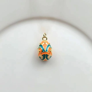 Detail of 18k gold plated egg pendant with orange and peacock blue enamel patterns