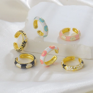 Detailed view of six adjustable enamel daisy rings in various colors on white silk