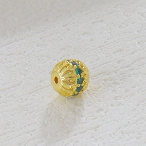 Detalle de un dije calado chapado en oro de 18k con piedras verdes para bisutería