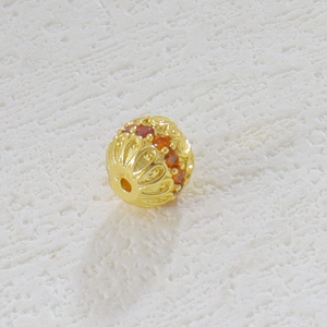 Detalle macro de un dije calado chapado en oro con piedras naranjas para joyería DIY