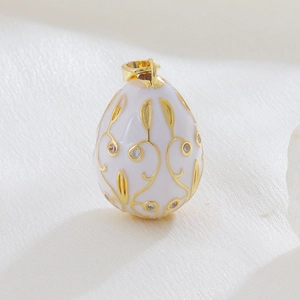Macro shot of egg-shaped pendant with white enamel, gold vines, and crystal inlay