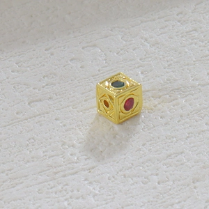 Vista macro de colgante de cubo chapado en oro de 18k con grabados y piedras de color