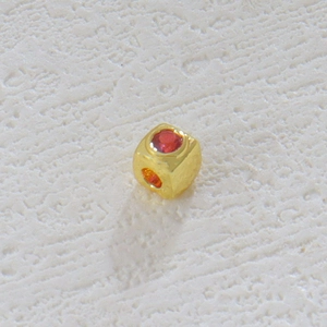 Primer plano de cuenta cúbica bañada en oro de 18k con una piedra preciosa roja redonda