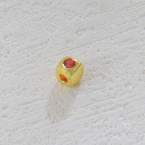Detalle macro de un dije de cubo chapado en oro de 18k con gema roja incrustada