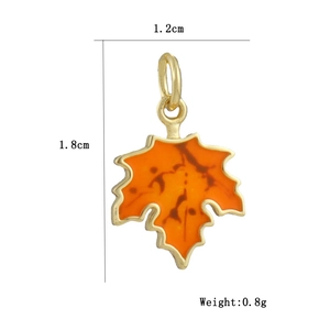 Detailed view of gold-plated maple leaf pendant with orange enamel, size 1.2cm by 1.8cm