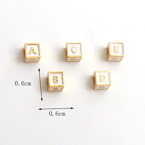 Detailed view of 6mm white enamel cube alphabet charms with gold plating and side holes