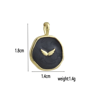 Macro detail of round 18k gold plated charm with black enamel and golden wings motif