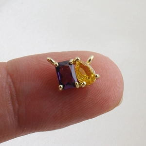 Detail of a mini gold-plated charm with a purple rectangle and yellow teardrop zircon stones
