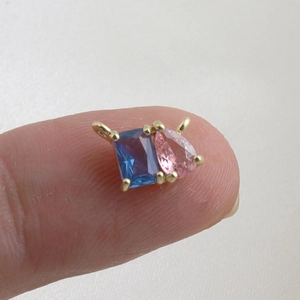 Macro view of mini water drop zircon pendant with blue and pink stones on a fingertip