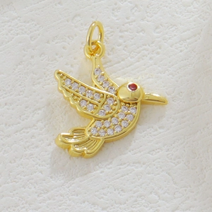 Detailed macro view of 18k gold hummingbird pendant with white crystals and red gem eye
