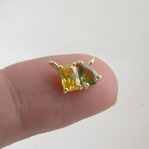 Macro view of a gold-plated pendant with square yellow and teardrop green zircon stones