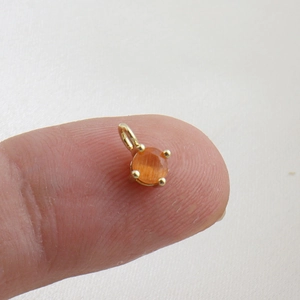 Close-up of a mini 18k gold plated pendant with an orange zircon stone on a fingertip