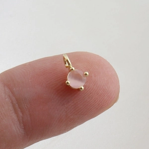 Macro shot of a mini round pink gemstone pendant held on fingertips for size reference