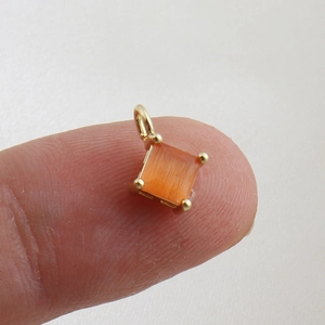 Macro shot of a mini square orange gemstone pendant held on a finger for size comparison