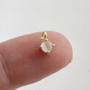 Detailed view of mini 18k gold pendant with moonstone held on fingertip for size scale