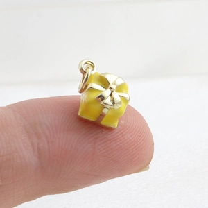 Mini pendentif boîte cadeau jaune avec nœud doré montré sur un doigt pour la taille