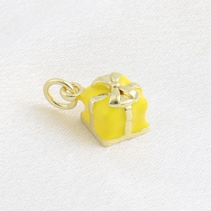 Détail d'un pendentif boîte cadeau en émail jaune avec ruban doré sur soie blanche
