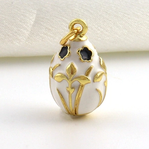 Detailopname van een witte emaille eivormige hanger met gouden Franse lelie patronen