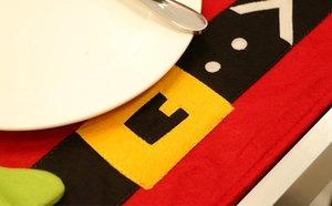 Detail of red felt Christmas table mat with Santa belt design and festive tableware