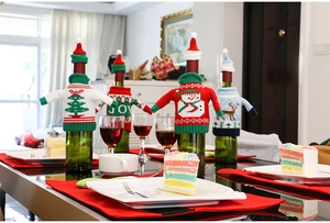 Close-up of four festive knitted Christmas wine bottle covers with mini hats and JOY pattern