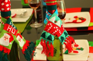 Detail of Christmas wine bottle cover with knitted scarf and Santa hat on table