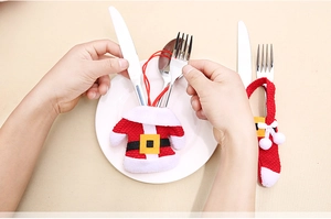 Placing silverware into Santa clothes cutlery holders on a white dinner plate decoration