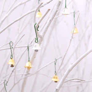 Christmas bell ornaments in gold and silver with green hooks on festive white branches