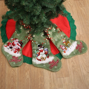 Three green burlap Christmas stockings with festive prints on a tree skirt background