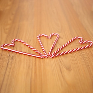 Three heart-shaped candy canes in red and white stripes on a rustic wooden background