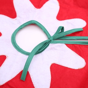 Red and white non-woven Christmas tree skirt with green ribbon ties and snowflake detail