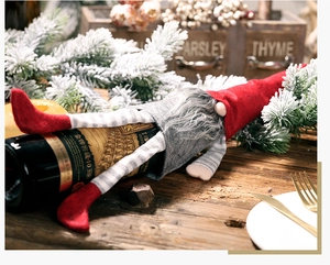 Detail of Christmas gnome wine bottle cover with long striped legs on wooden table