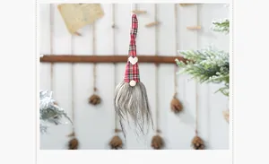 Detail of Christmas gnome ornament with red plaid hat and white heart hanging on pine branch