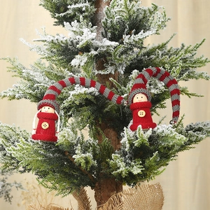 Detail of hanging Christmas gnome plush ornaments with striped hats on a snowy tree