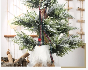 Détail d'un gnome de Noël avec chapeau à carreaux et cœur rouge sur une branche enneigée
