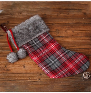 Detail of red plaid Christmas stocking with grey faux fur trim and plush balls on wood
