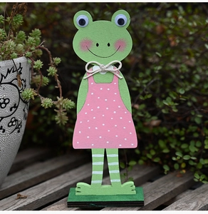 Detail van houten paaskikkerbeeldje met roze polkadotjurk tegen een groene tuinachtergrond