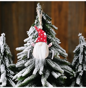 Hanging wooden Christmas gnome with red heart hat and silver star on snowy tree branch