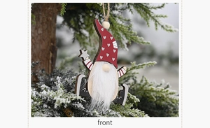 Close-up of wooden Christmas gnome ornament with red heart hat on a snowy pine branch